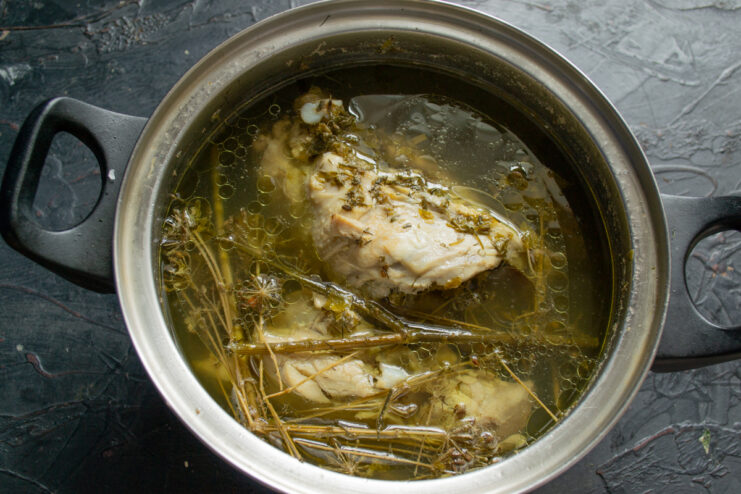 Cooking the chicken broth Chicken simmering in a pot with fresh herbs, garlic, and whole spices