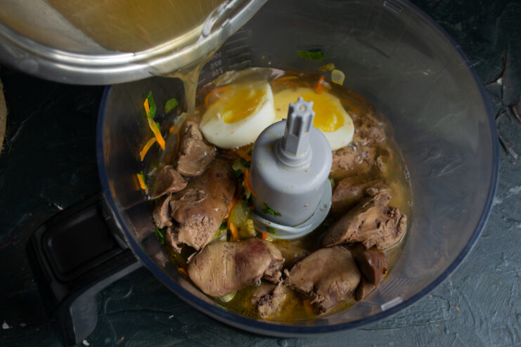 Adding the broth Pouring gelatin broth into a blender jar with chicken liver and vegetables.