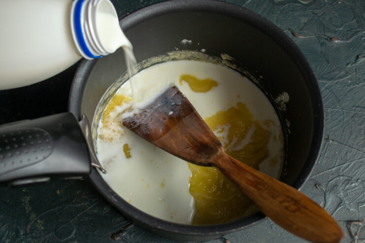 Creating the Creamy Base Milk being poured into a saucepan with roux while whisking continuously.