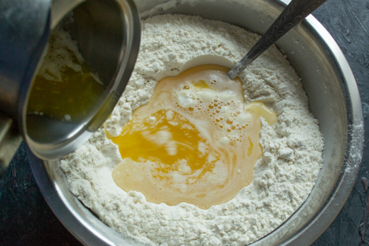 Pouring cooled melted butter and egg mixture into a well in the flour