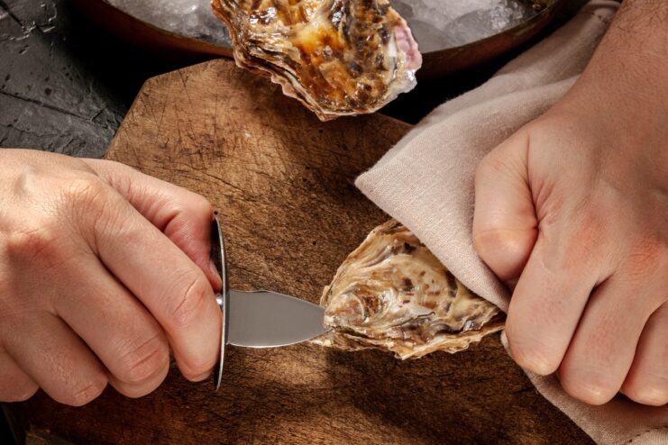 Inserting Knife Into Oyster Hinge Close-up of inserting a shucking knife into the hinge of a fresh oyster