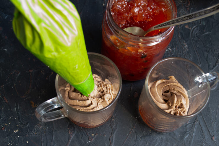 Piping chocolate ricotta cream into a clear mug over the jam.