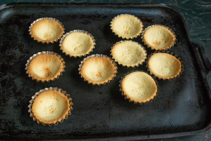 Baking the tartlets until golden brown Baked golden shortcrust pastry shells on a black baking tray