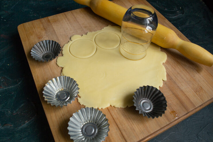 Cutting dough circles for the tartlets Cutting circles from the rolled dough using a glass next to metal molds