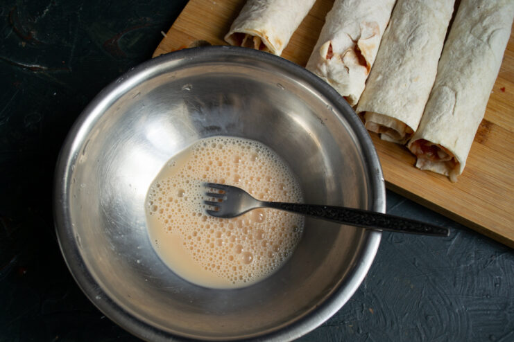Whisking an egg and milk mixture in a bowl to coat the rolls