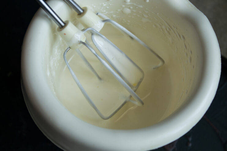 Whisking eggs with sugar. Whisking eggs with sugar using a hand mixer in a tall white bowl.