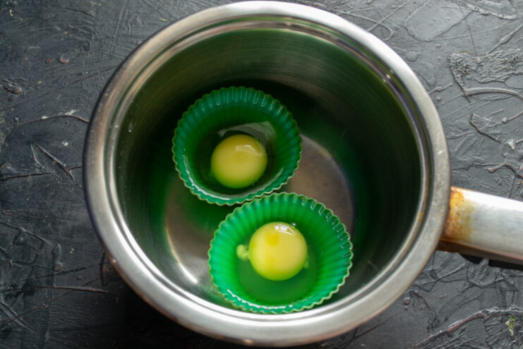 Poaching Eggs Without Vinegar Raw eggs in silicone muffin liners cooking in a simmering water bath