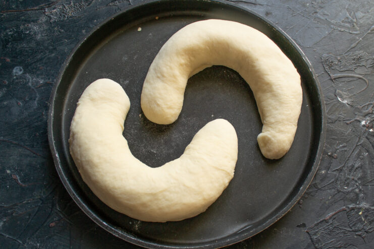 Unbaked crescent-shaped dough arranged on a baking sheet with space between them