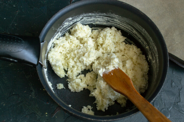 Cooking the coconut dough on the stove. Thickened coconut dough gathering into a ball in a saucepan.