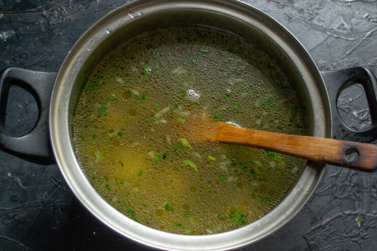 Boiling the soup base Pouring clear hot chicken broth over vegetables and rice in a cooking pot