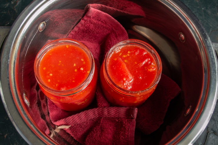 Pouring hot juice over the chopped tomatoes Pouring hot tomato juice into glass jars filled with chopped tomatoes