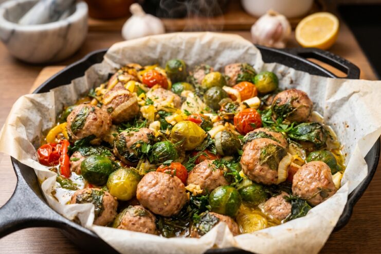 Oven-baked meatballs with Brussels sprouts and cherry tomatoes in a cast-iron skillet.