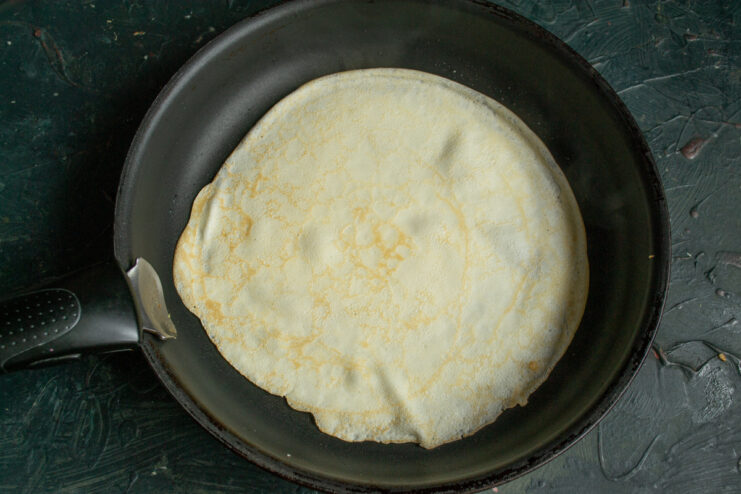 Thin crepe batter cooking in a hot skillet