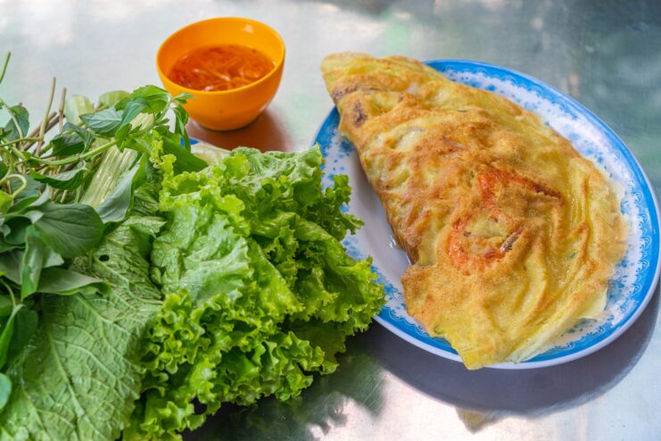 Crispy yellow banh xeo crepe with fresh herbs Crispy yellow banh xeo crepe stuffed with shrimp served alongside fresh greens.