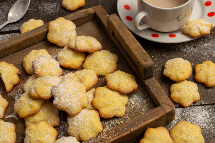 Golden polenta cookies served on a wooden tray alongside a cup of coffee.