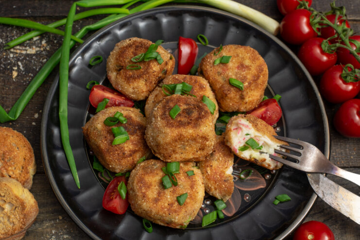 Golden imitation crab croquettes served with vegetables on a dark plate