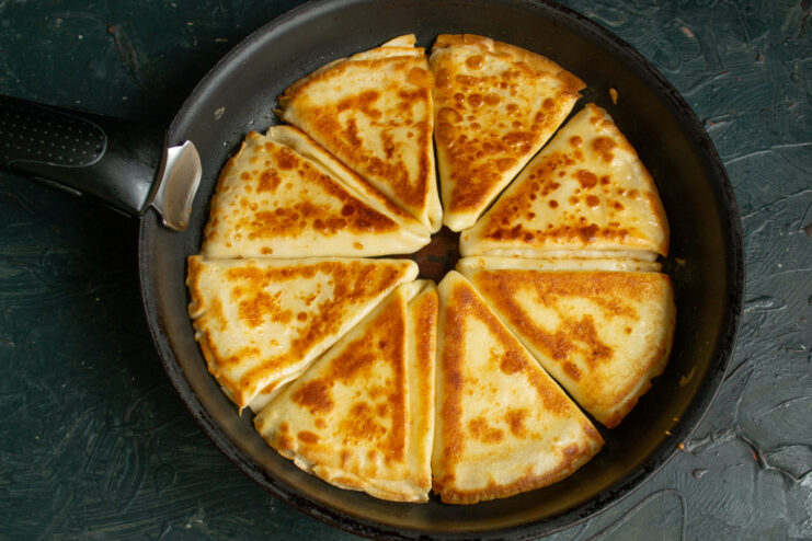 Golden brown folded crepes sizzling in a pan