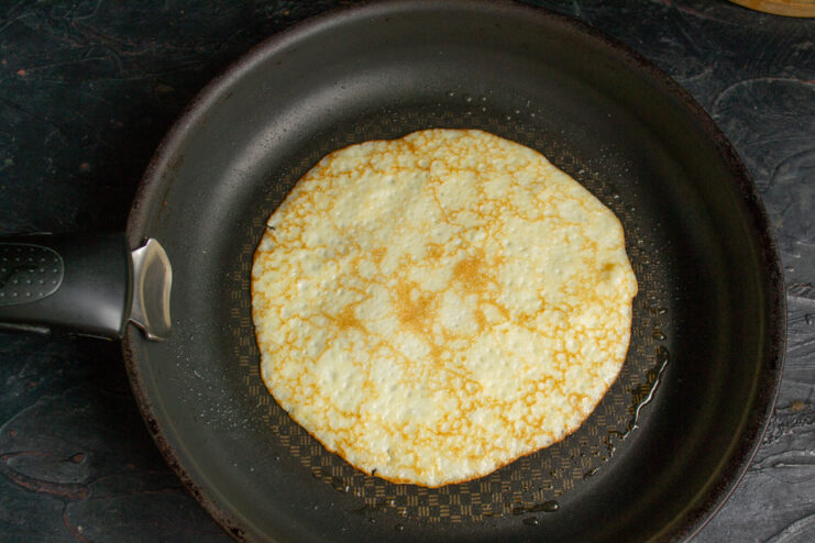 Golden brown zucchini crepe cooking in a black frying pan