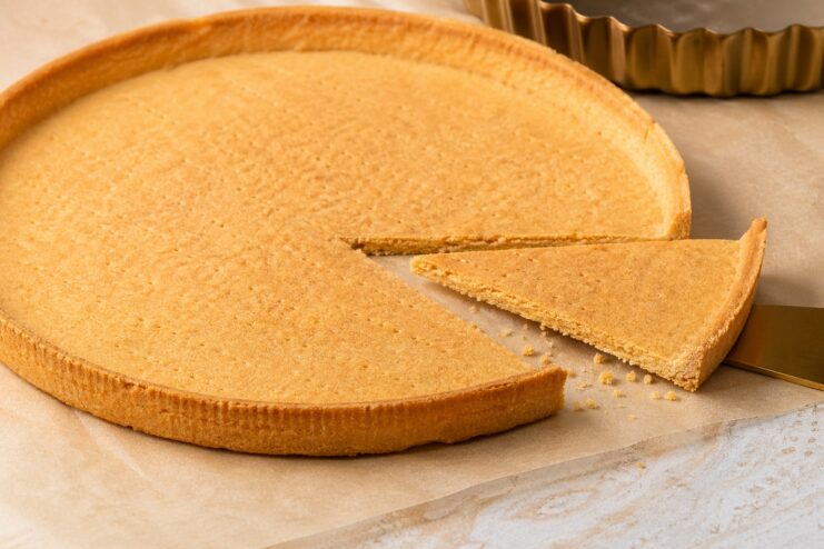 Perfectly baked shortcrust tart shell Golden shortcrust tart shell on a dark surface with a single slice removed.