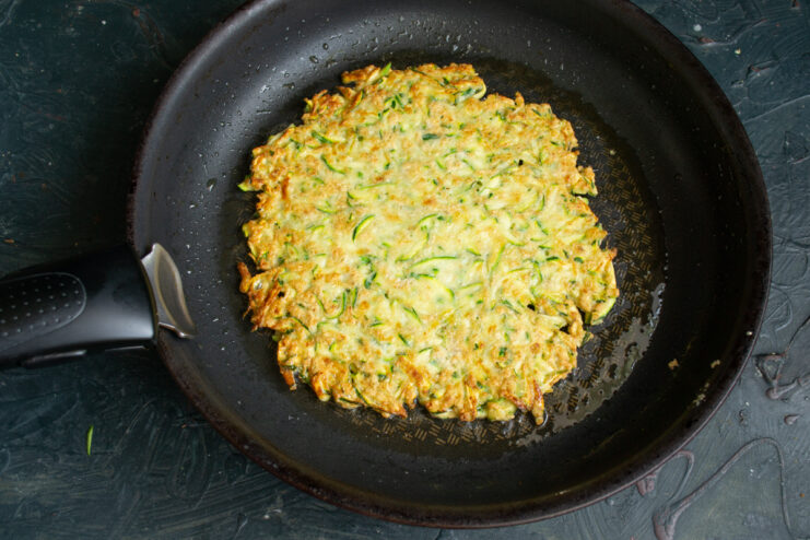 Searing the pancake Frying a golden zucchini pancake in a skillet.