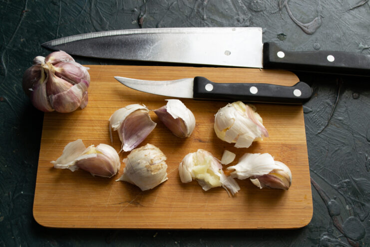 Crushing Garlic Cloves Garlic cloves on a wooden cutting board next to kitchen knives.