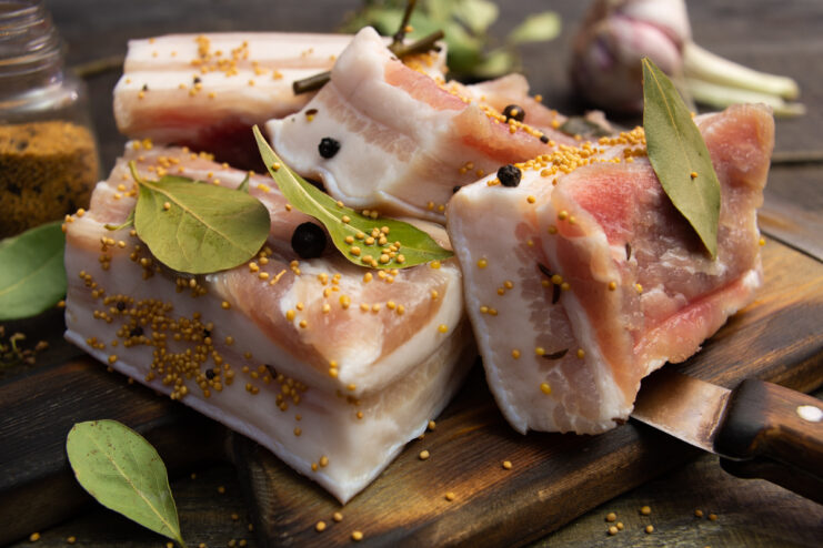 Appetizing wet-cured salo with mustard seeds and bay leaf on a wooden cutting board
