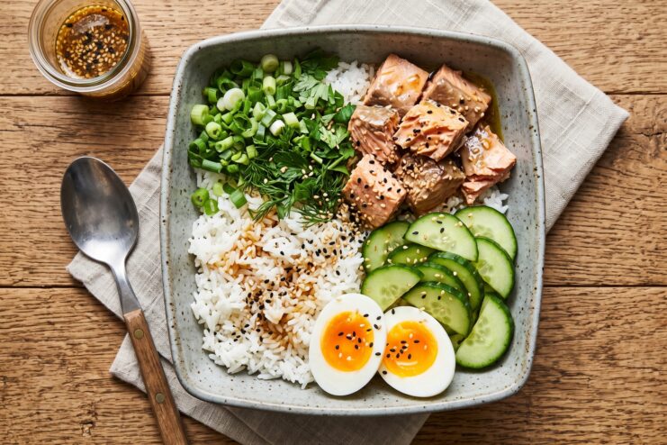 Asian-style rice bowl topped with fish chunks, fresh cucumber, egg, and green onions