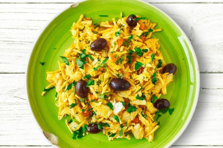 Classic Bacalhau à Brás served on a green plate and garnished with black olives