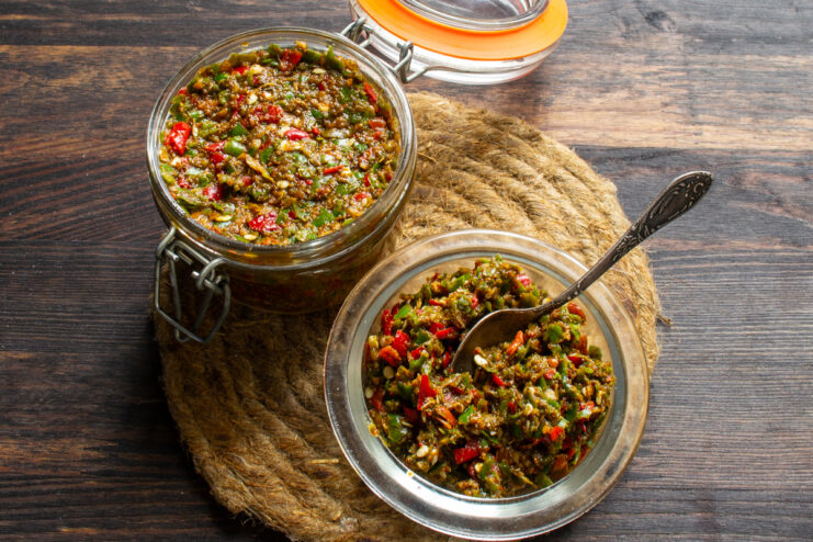 Serving ready adjika Glass jar and a bowl of ready adjika on a jute coaster against a dark wooden background.