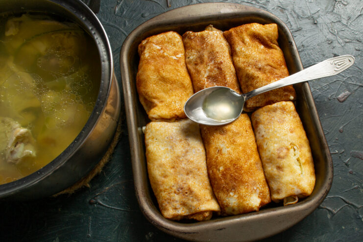 Crepes Soaking In Chicken Broth Stuffed crepes in a baking dish covered with hot chicken broth