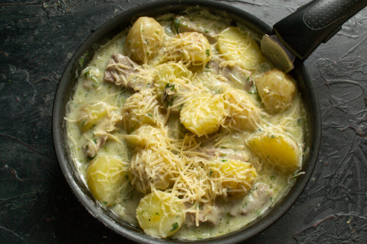 Sprinkling with cheese Grated cheese sprinkled over potatoes and ribs in a skillet