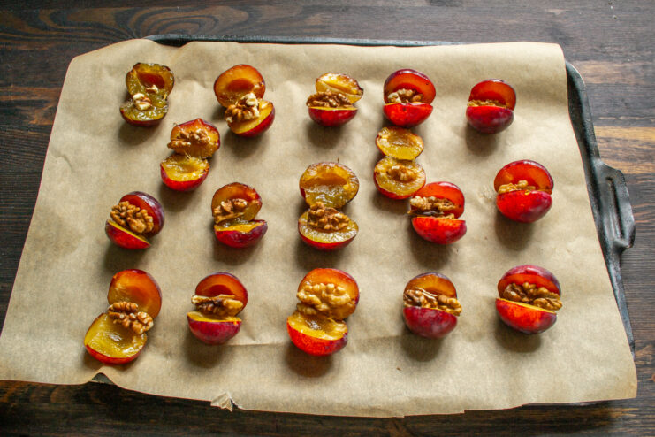 Walnut quarters neatly tucked inside fresh plum halves on a baking sheet