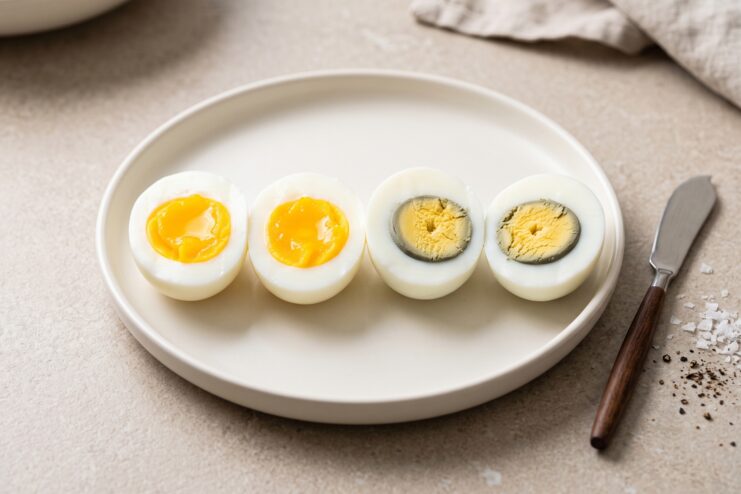 Comparison of Yolk Doneness Four boiled egg halves displaying various yolk consistencies from runny to overcooked.