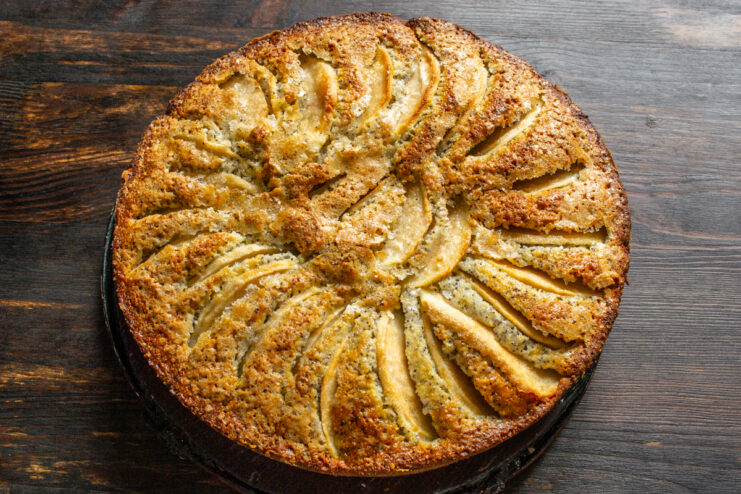 Removing the cake from the baking dish Whole finished apple and poppy seed cake placed on a dark surface