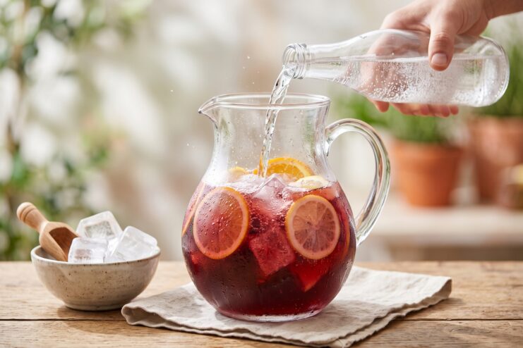 Pouring sparkling water into a pitcher filled with red sangria