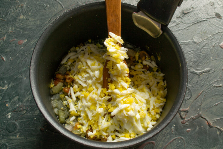 Adding Eggs To The Filling Mixing chopped hard-boiled eggs into the cooked chicken cracklings