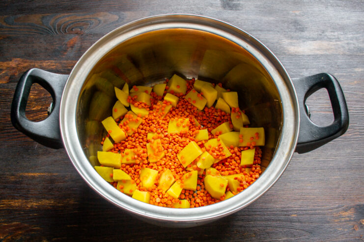 Adding plant-based protein Adding red lentils to the diced potatoes in the pot