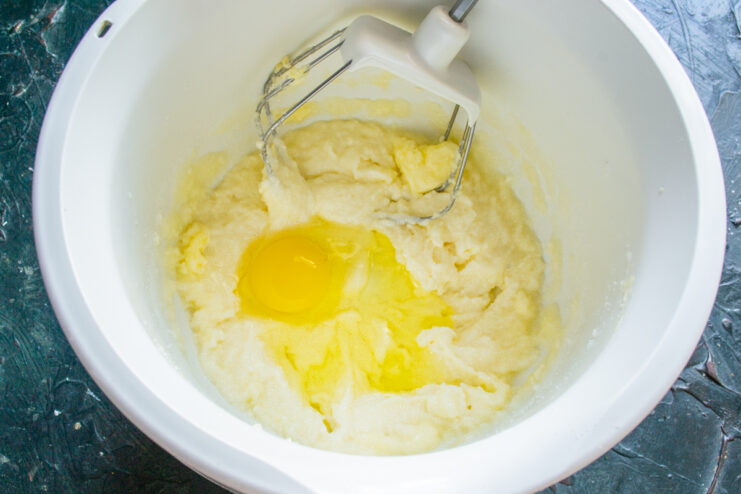 Adding eggs to the batter Adding an egg into the creamed butter mixture