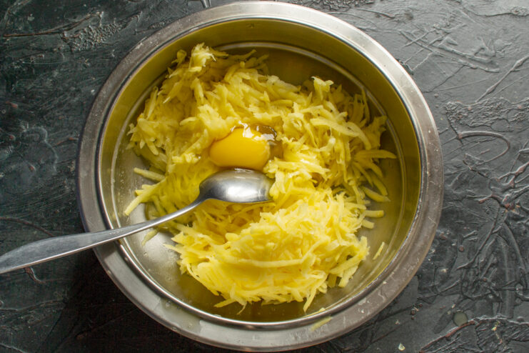 Adding eggs to bind the mixture Cracking a raw egg into a bowl of grated potatoes