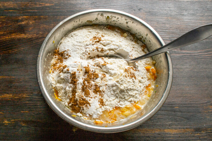 Incorporating dry ingredients and spices Adding all-purpose flour, baking powder, and warm spices to the wet muffin mixture.