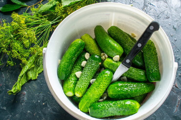 Adding garlic to the pickles Scattering sliced garlic cloves over cucumbers in a bucket
