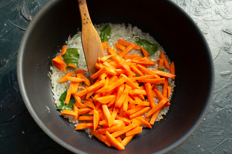 Adding thick carrot batons to sautéed onions in a skillet