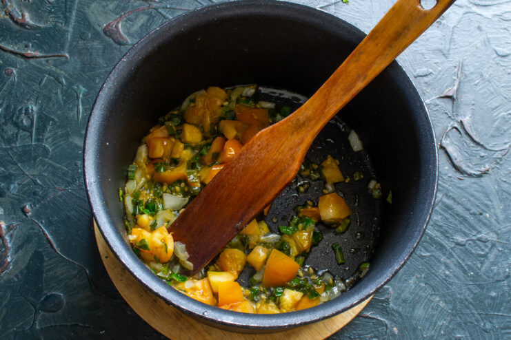 Adding diced yellow tomatoes to sautéed green onions in a saucepan