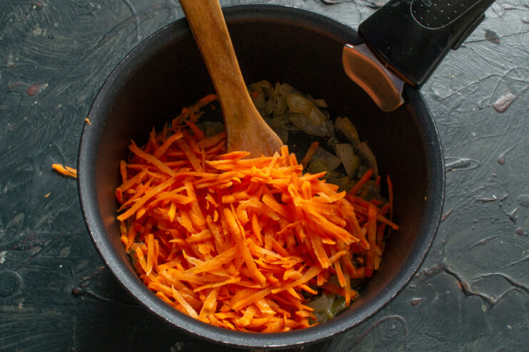 Adding the carrots Adding grated carrots to the sautéed onions inside a cooking pot.