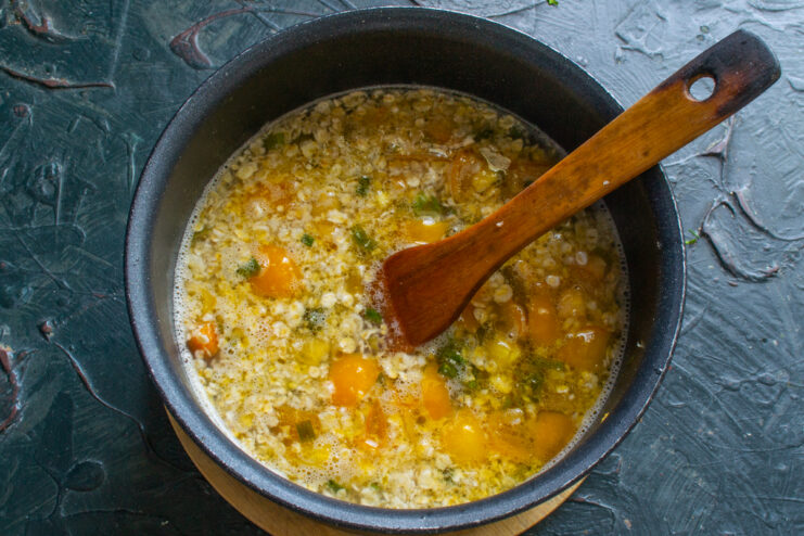 Stirring quick-cooking rolled oats into a simmering vegetable soup base