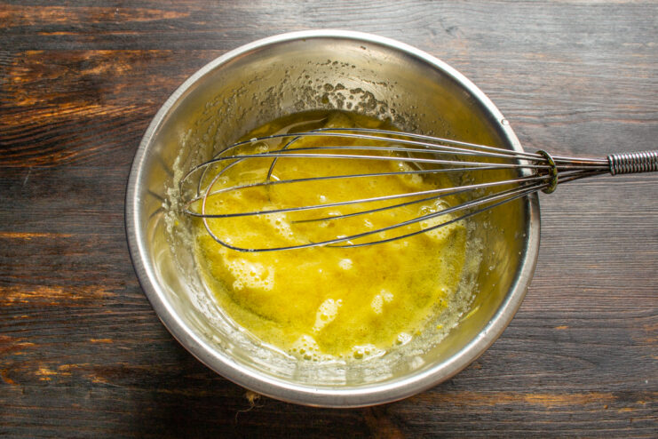 Adding melted butter to the batter Pouring cooled melted butter into a bowl with the beaten egg and sugar mixture.