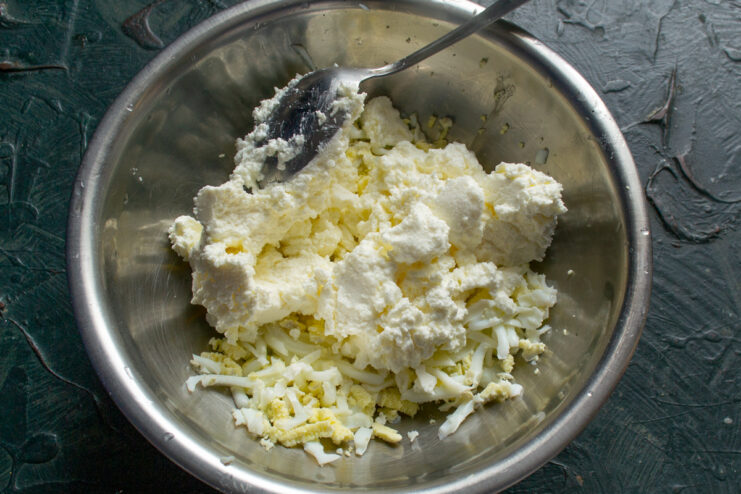 Adding soft cream cheese Adding cream cheese to grated eggs in a mixing bowl
