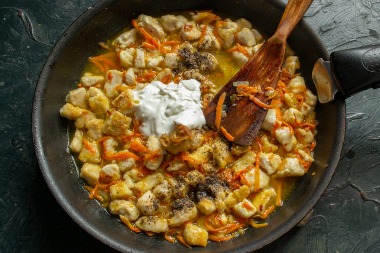 Preparing the sauce Stirring sour cream and broth into the simmering chicken ragout
