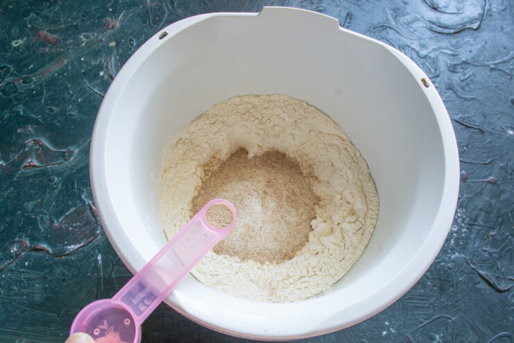 Adding The Yeast Adding dry instant yeast into the flour mixture using a measuring spoon.