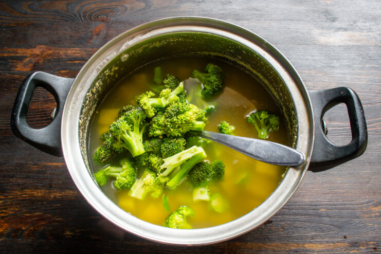 Adding broccoli to the borscht Dropping fresh green broccoli into the simmering soup